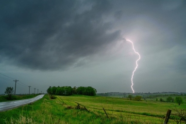 An image of a storm with lightning hitting the ground of a rural scenery. 